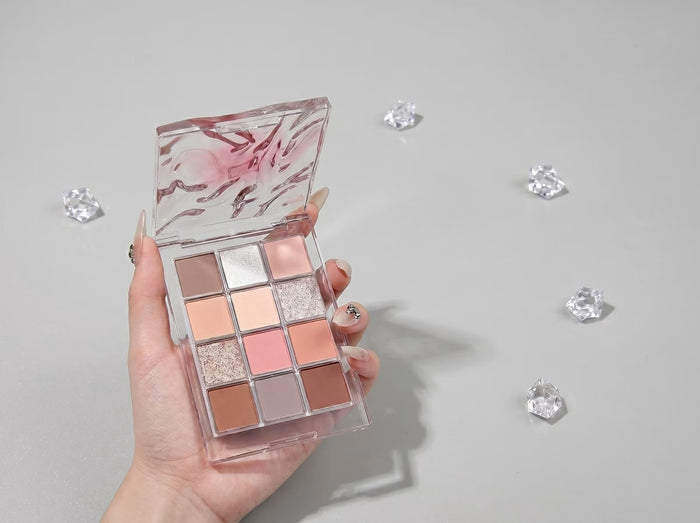 nude eyeshadow palette held by a hand against grey background with diamons used as props 