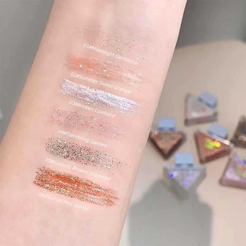Color swatches on a wrist with glittery shades of Eyeshadow palette and small containers in the background.
