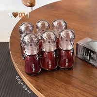 Red and clear lip glosses bottles with 'Gege bear' branding on a wooden table.