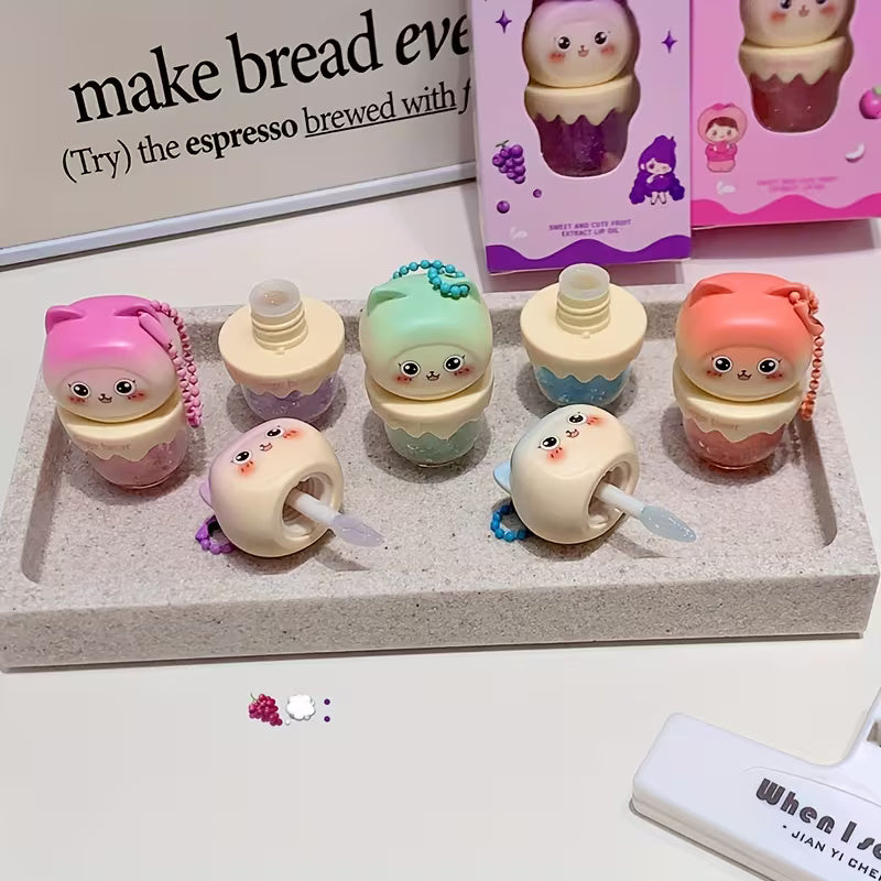 Clear lip oil in a sleek tube shown with a glossy applicator, reflecting a soft, luminous shine. The product appears lightweight and moisturizing, suggesting smooth, hydrated lips with a natural, non-sticky finish.