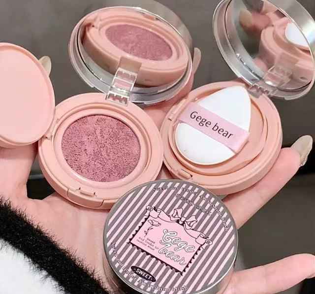 Makeup compact with pink blush and white puff, held by a hand.