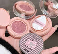 Makeup compact with pink blush and white puff, held by a hand.