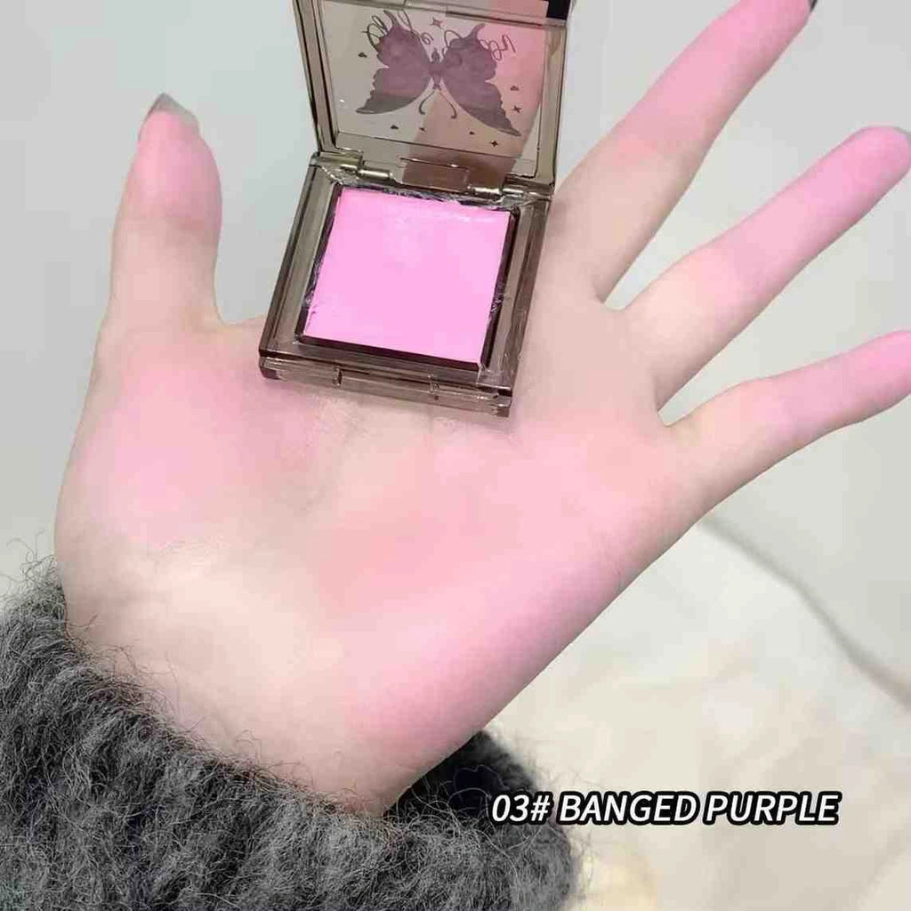 Hand holding a pink makeup product with a butterfly design on the case, labeled '03# BANGED PURPLE'.
