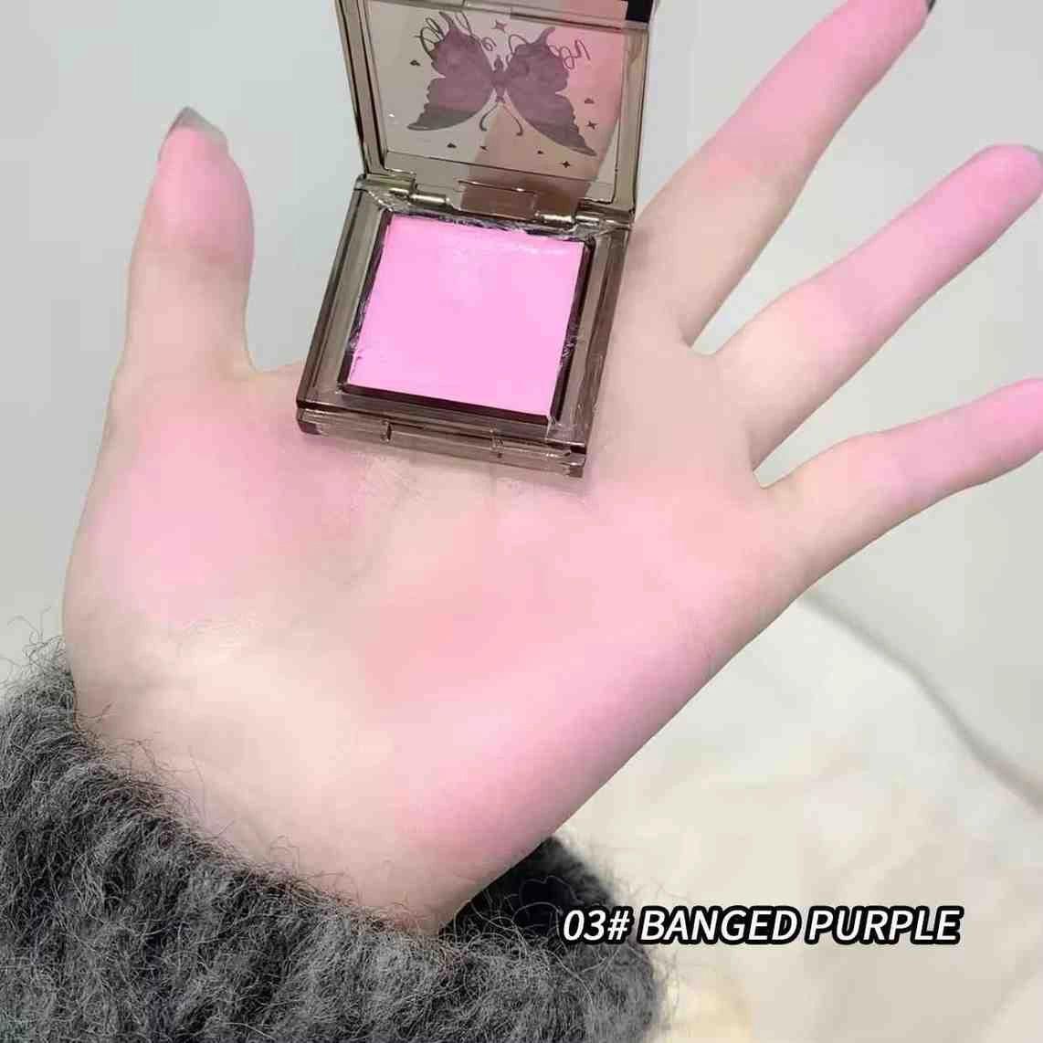 Hand holding a pink makeup product with a butterfly design on the case, labeled '03# BANGED PURPLE'.