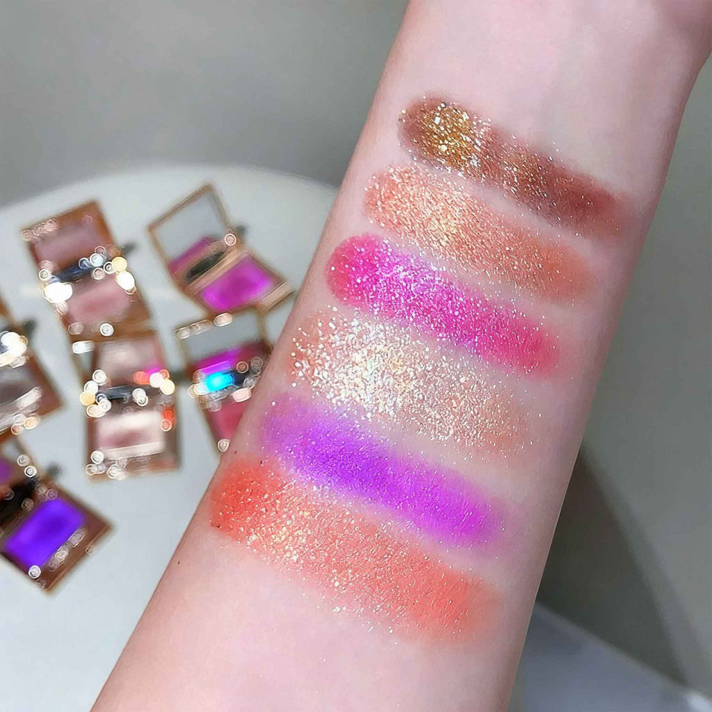 Colorful Eyeshadow swatches on a person's arm with small open makeup cases in the background.
