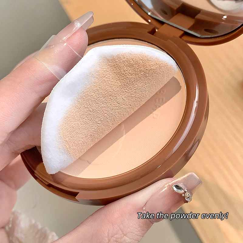 Compact powder with a white puff held by a hand on a wooden surface.