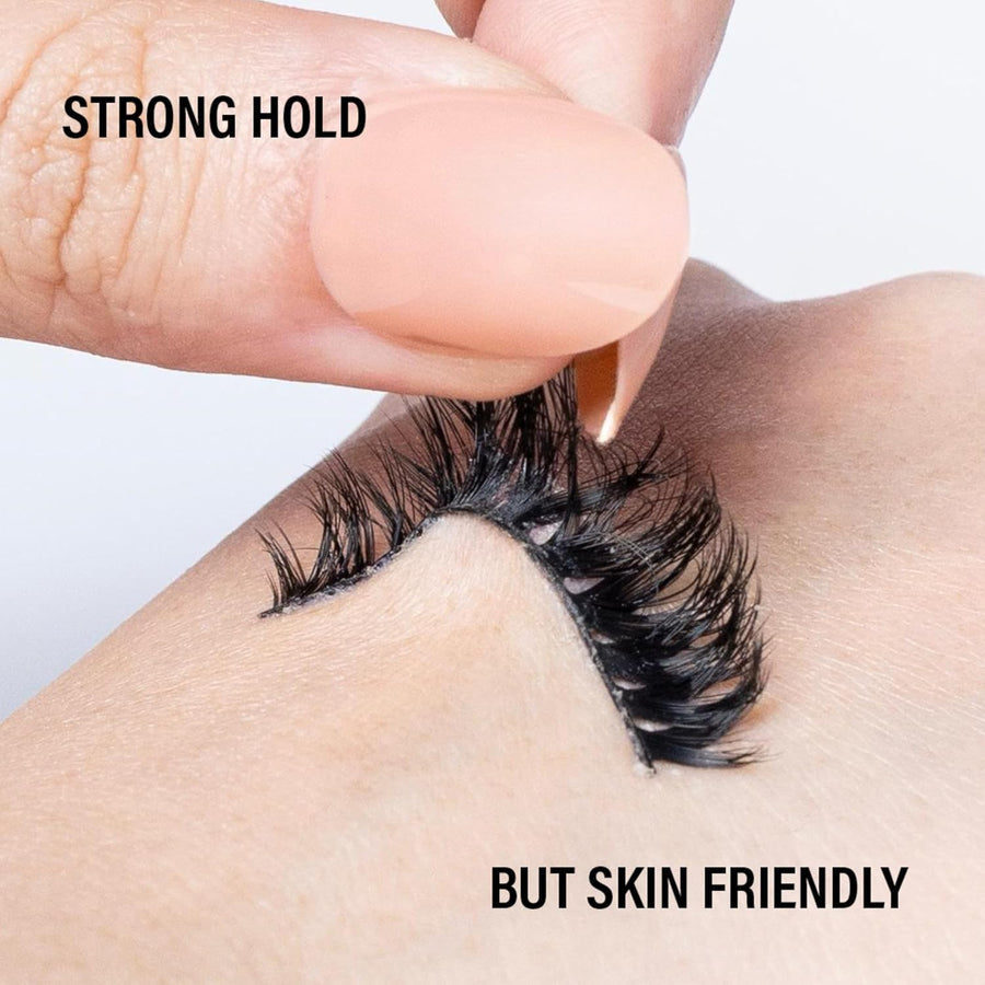 False eyelashes being applied with a finger, text 'STRONG HOLD' and 'BUT SKIN FRIENDLY' on a plain background.