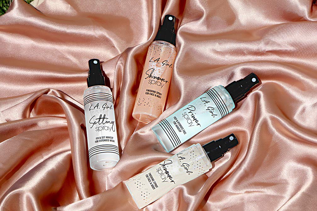 Four L.A. Girl spray bottles on a pink satin background