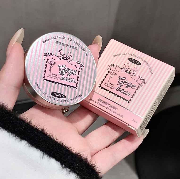 Pink makeup compact and its packaging held in a hand against a gray background