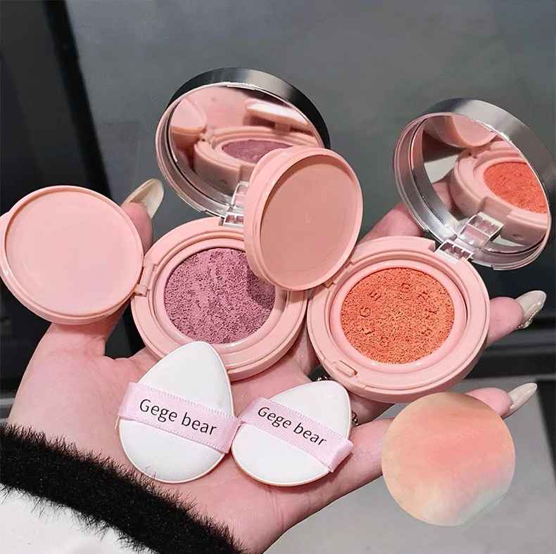 Compact makeup products with open cases showing blushes and a powder puff, held by a hand.