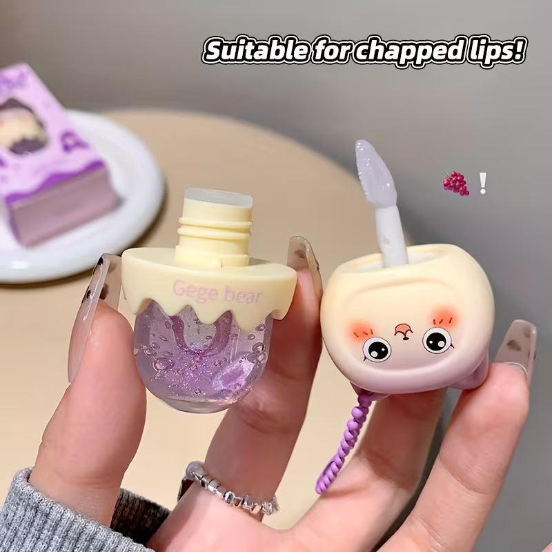 Clear lip oil in a sleek tube shown with a glossy applicator, reflecting a soft, luminous shine. The product appears lightweight and moisturizing, suggesting smooth, hydrated lips with a natural, non-sticky finish.