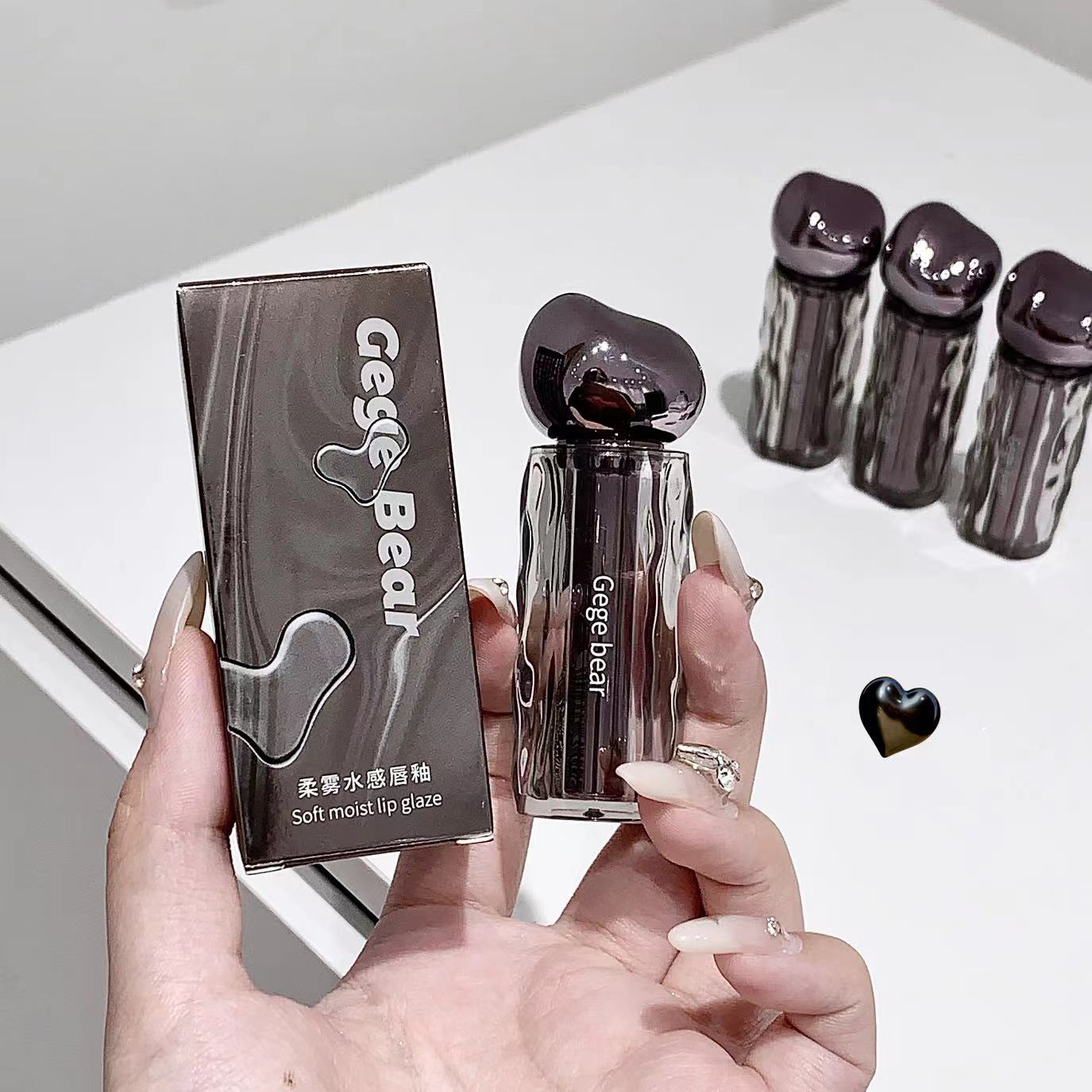 Hand holding a Gege Bear lip gloss with packaging and additional lip glosses in the background.