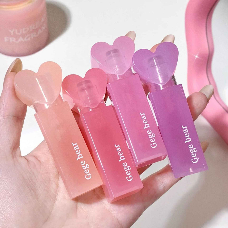 Hand holding four pink lip balms with 'Geege bear' branding on a light background