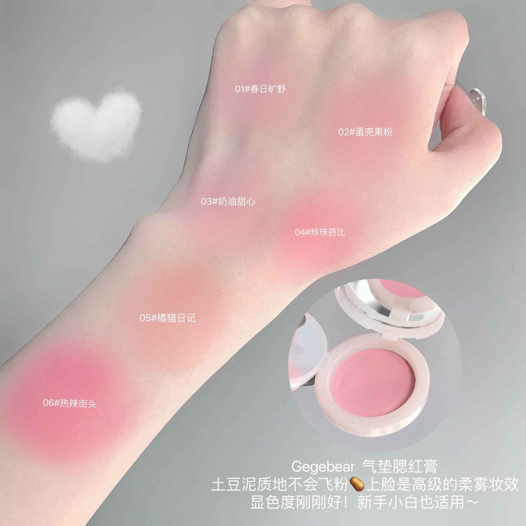 Hand swatching blush on a gray background with product packaging.