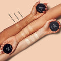 Hands holding e.l.f. foundation pots with swatches on a beige background