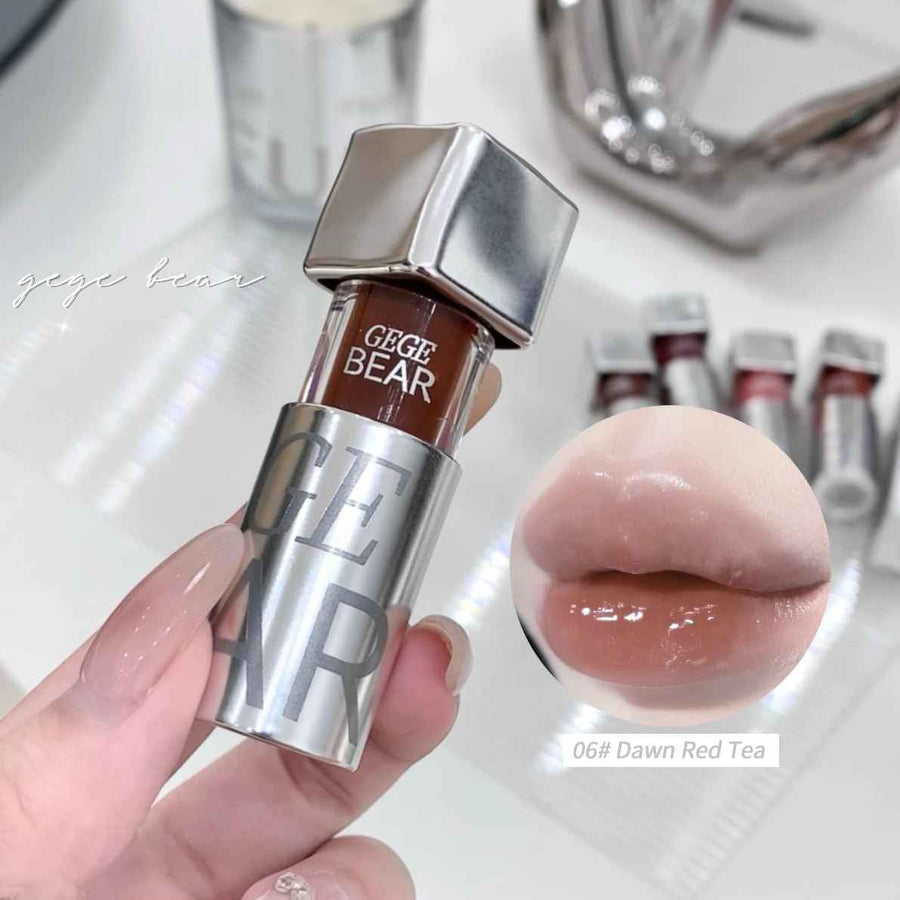 Lip gloss held by a hand with a close-up of a lip, on a blurred background with 'GEGE BEAR' branding.