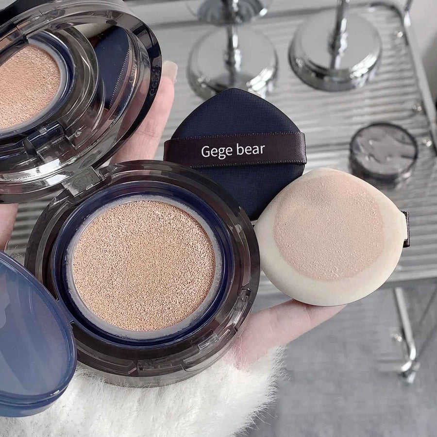 Makeup foundation with powder and puff, branded 'Gege bear', on a blurred background.
