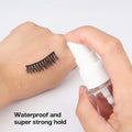 Person applying eyelash adhesive to false eyelashes with a small bottle on a white background.