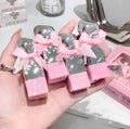 Pink and silver heart-shaped boxes of lipsticks with bows held in a hand, with 'GEGEBEAR' branding in the background.