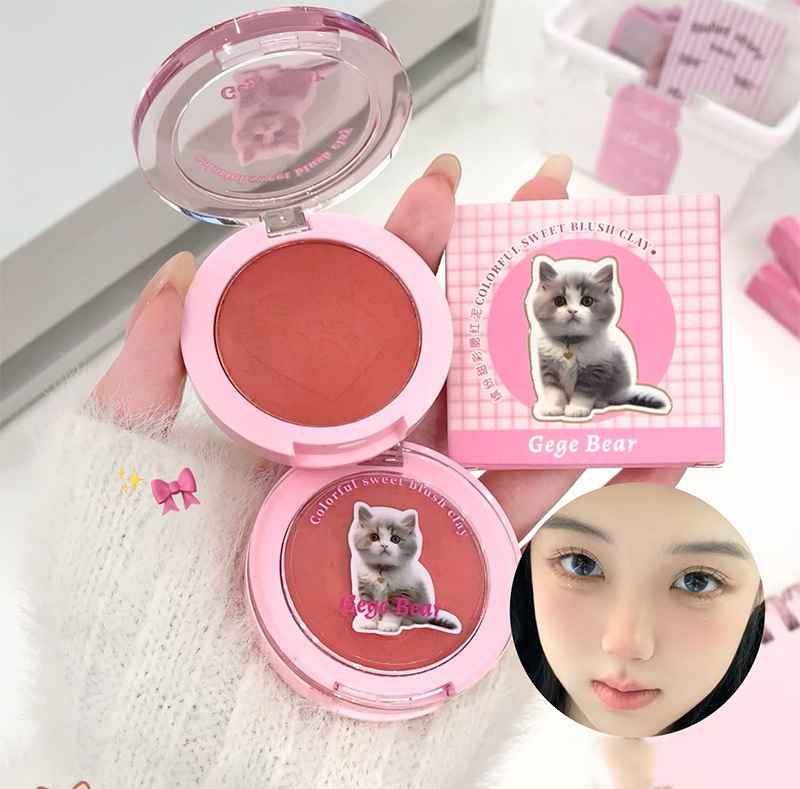Pink blush compact with a cat design on the lid, held by a hand.