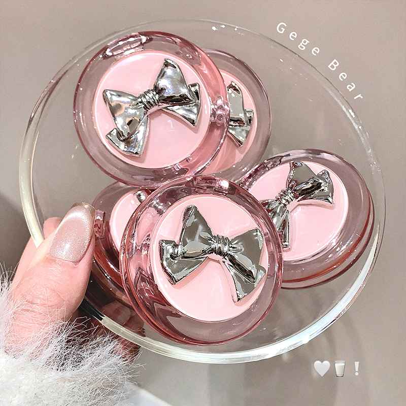 Pink compact blush and mirrors with silver bows held by a hand on a light background