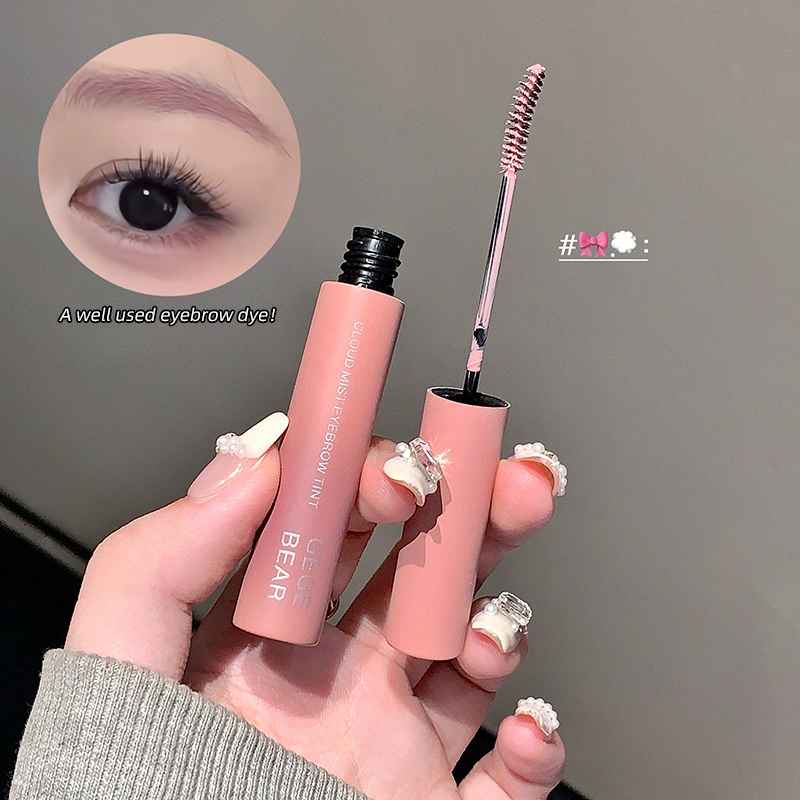 Pink eyebrow with applicator held by a hand, close-up of applied eyebrow color on eye.