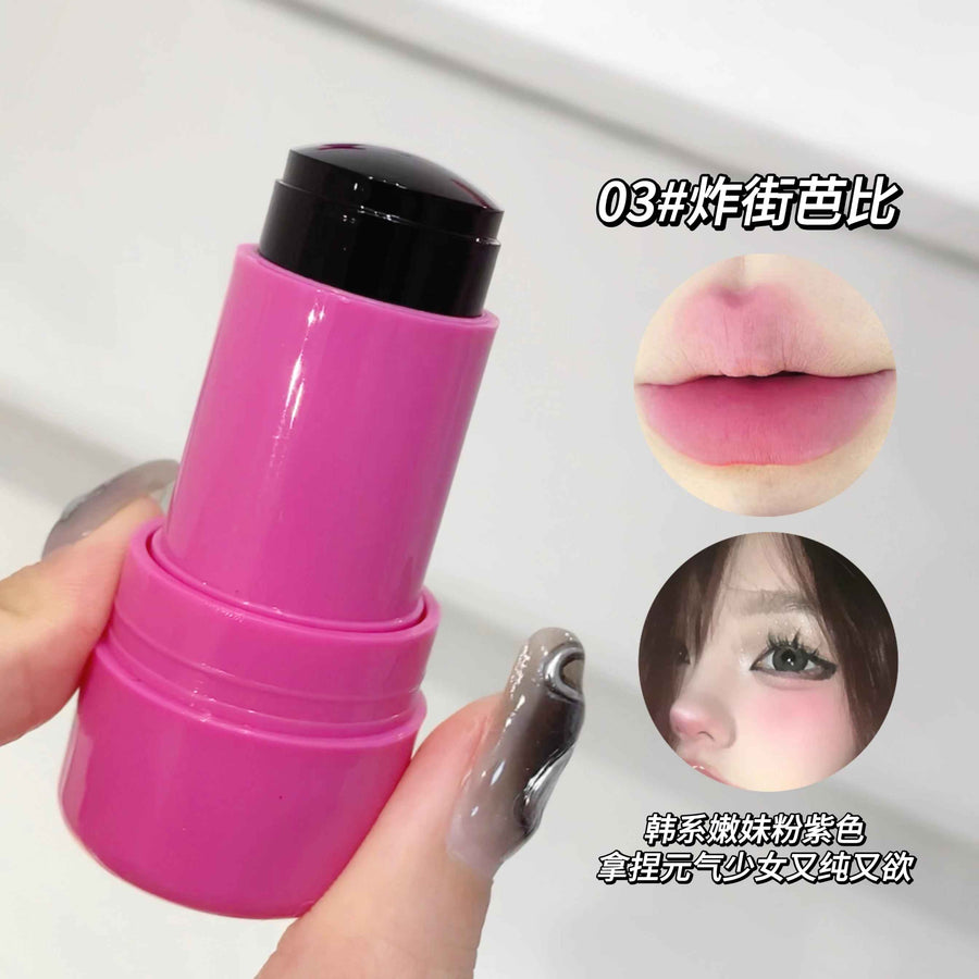 Pink lip balm with black cap held by a hand, close-up on a white background.