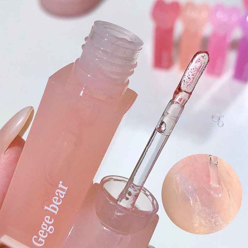 Pink lip gloss with applicator held by a hand, close-up view.