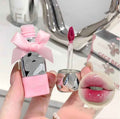 Pink lipstick with a bow held by a hand, close-up on a reflective surface.