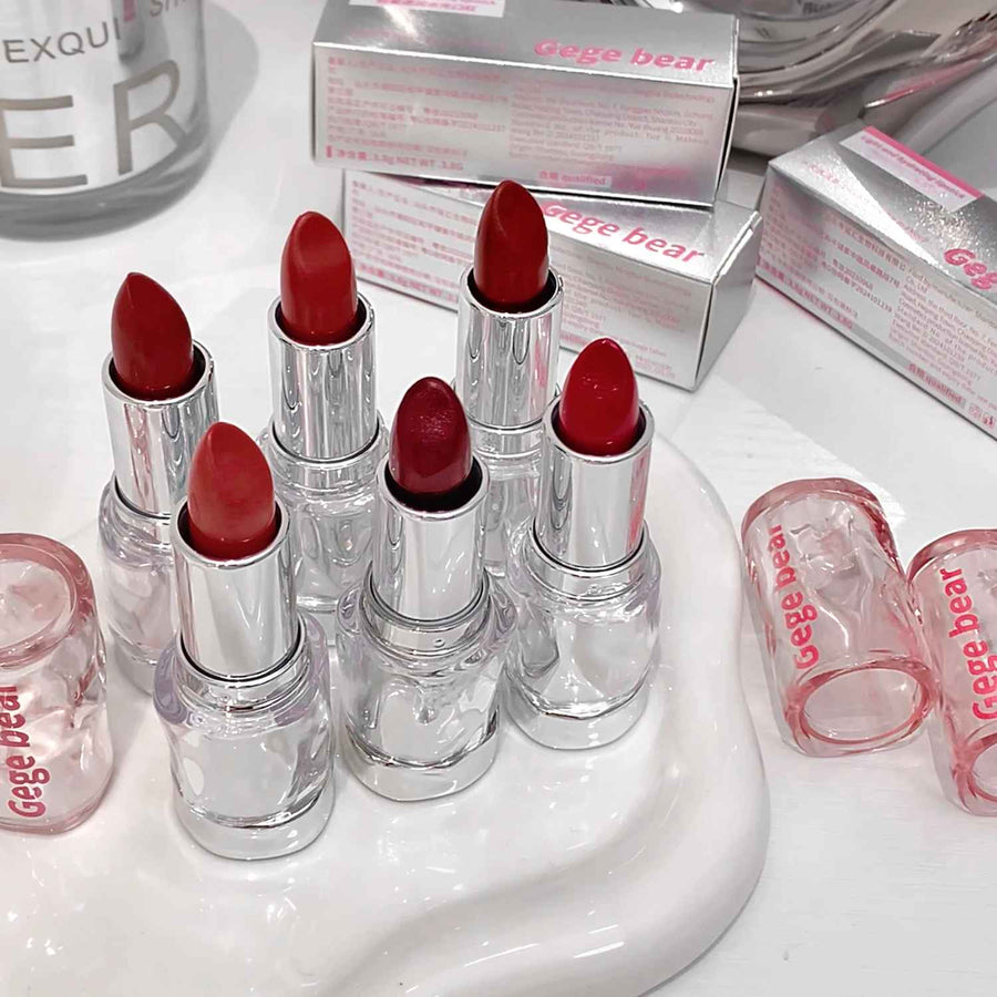 Red lip gloss with clear casings on a white surface, surrounded by 'Geege bear' boxes.