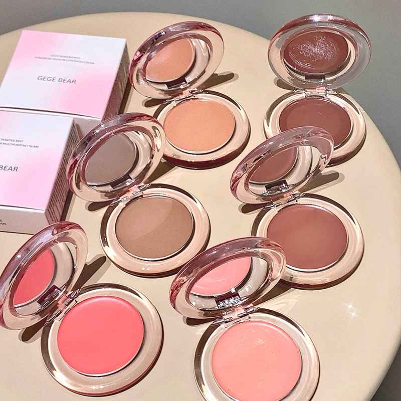Set of makeup blushes in various shades on a round surface with a pink box in the background.