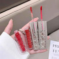 Hand holding a set of red lip glosses with a clear case.