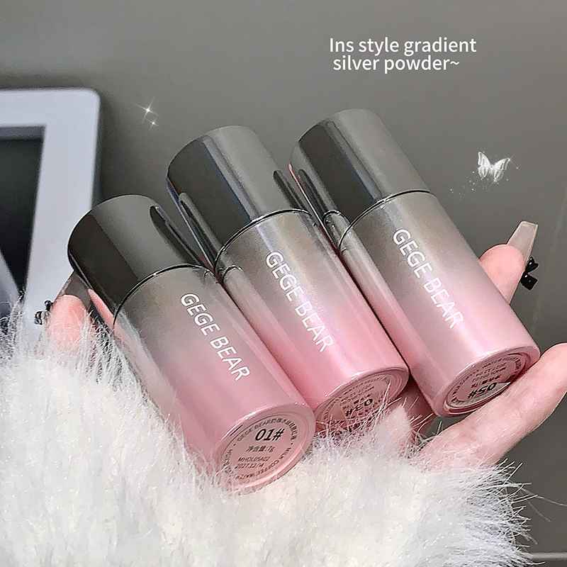 Three GEGE BEAR lip glosses with gradient effect held by a hand on a textured surface.