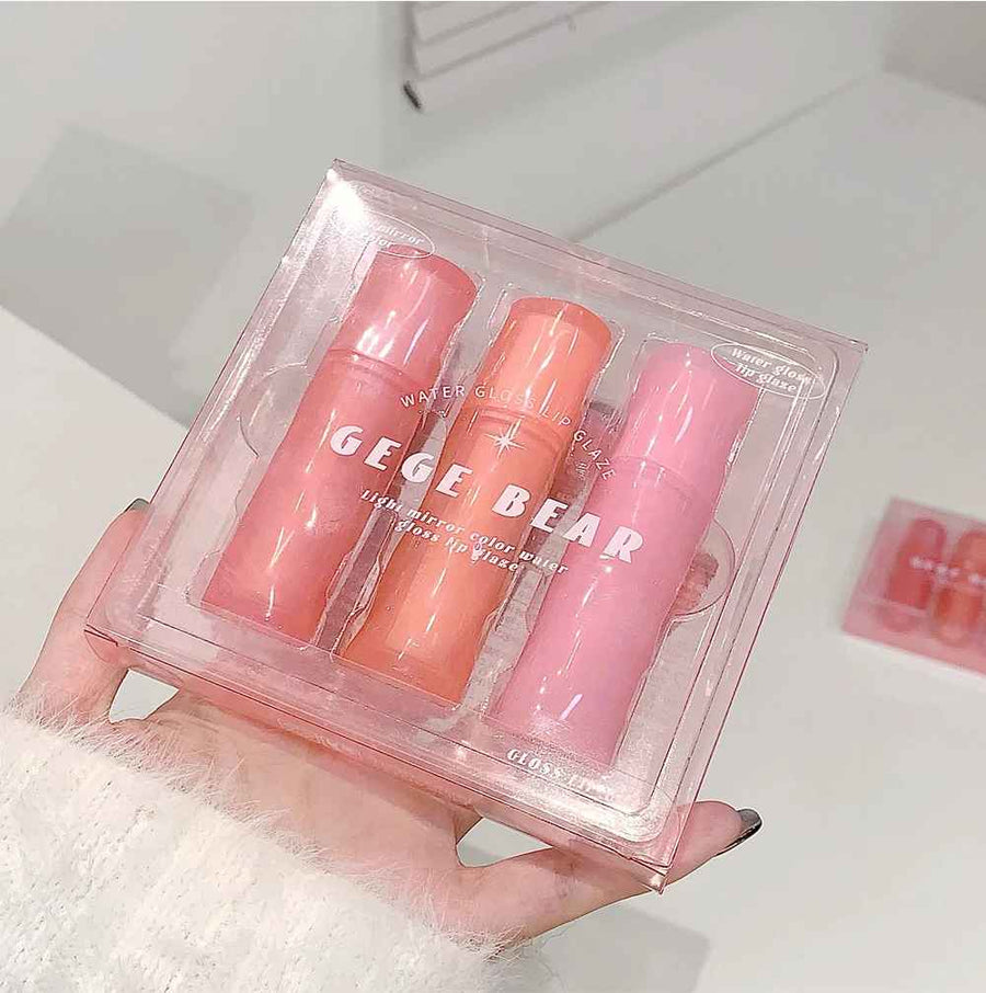 Three lip glosses in pink packaging held by a hand with a white fur sleeve.