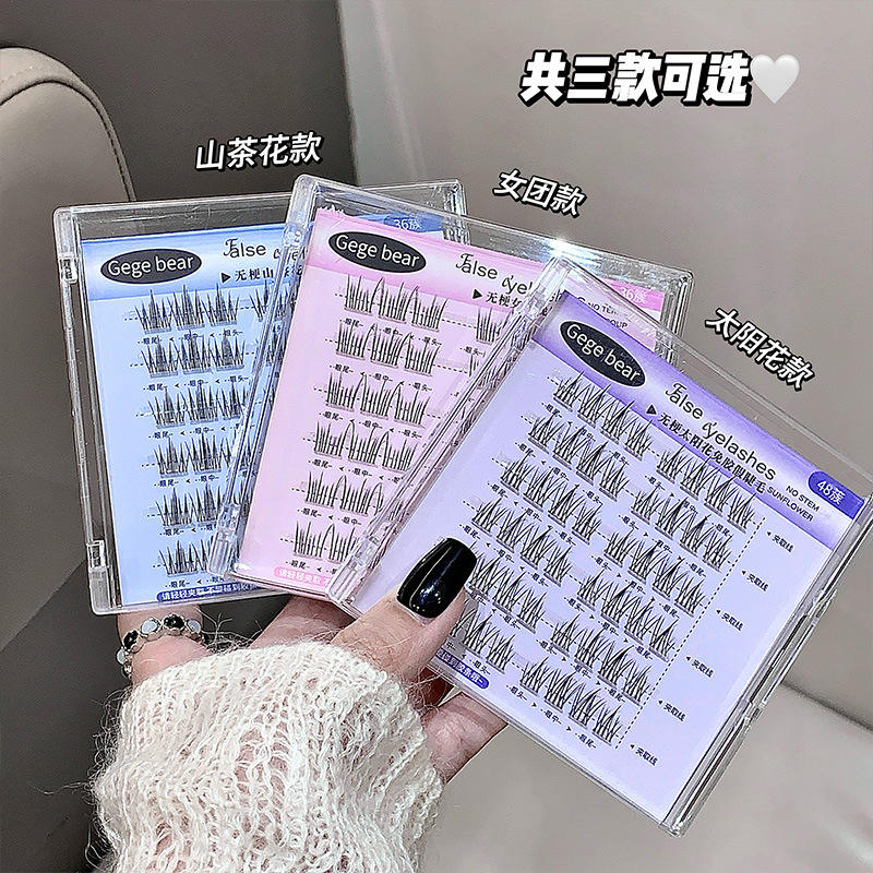 Three packages of false eyelashes held by a hand with black nail polish, against a neutral background.