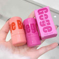 Two blush sticks and their packaging held in a hand with a white background