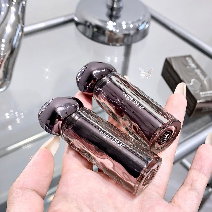 Two gege bear lip glosses held in a hand with a blurred background
