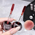 Two lip gloss applicators with a close-up of a lip swatch on a neutral background