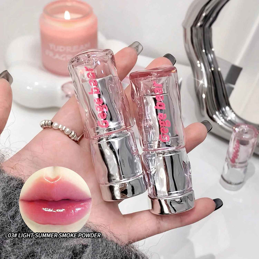 Two lip glosses held in a hand with a close-up of lips wearing the product, set against a blurred background.
