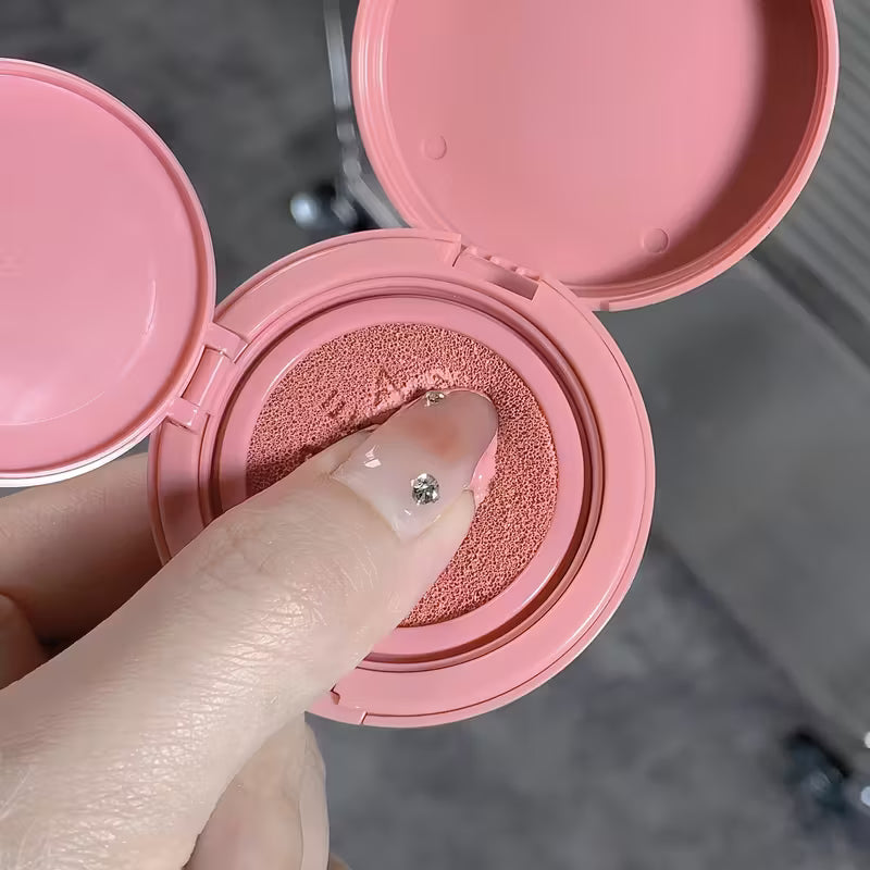 Pink makeup blush with a finger applying blush, blurred background