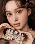 A close-up of a girl holding Flowerknows Sweetie Bear eyeshadow palette with both hands, showcasing swatches of the romantic nude pink and warm neutral matte shades pigmented on her skin.