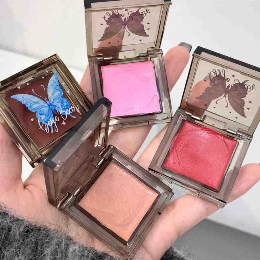 Four compact blushes with butterfly designs on the case held in a hand.