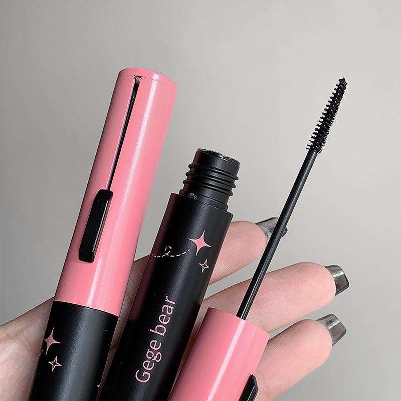 Two mascara tubes, one pink and one black with 'Gege bear' branding, held by a hand against a neutral background.