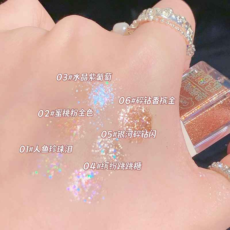Close-up of a hand with glittery makeup and a Eyeshadow palette container labeled with color names.