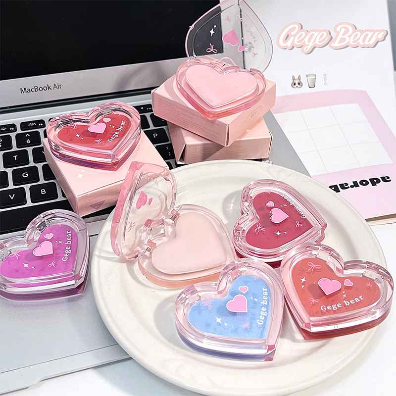 Heart-shaped pink lip balm with 'Gee Bear' branding on a white plate, laptop, and notebook in the background.