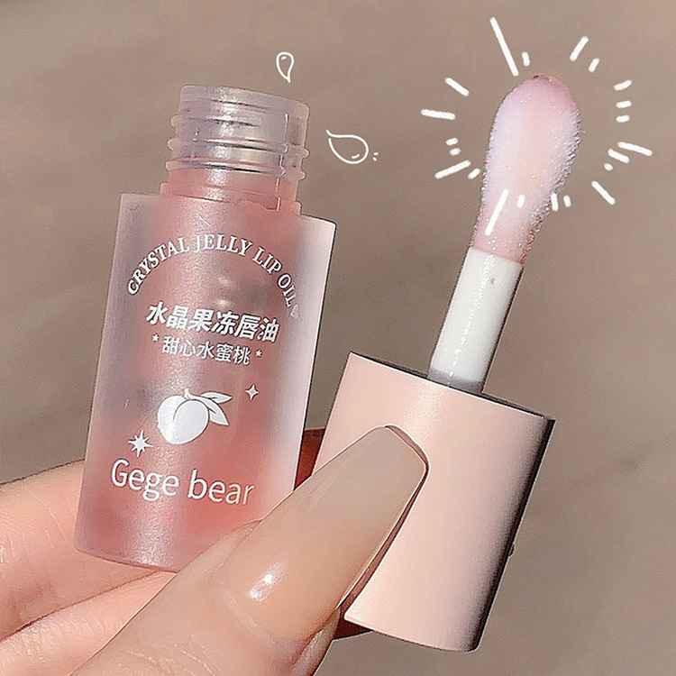 Pink lip oil with applicator held by a hand against a neutral background