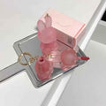 Pink lipstick with keychain on a white surface with a mirror reflection.