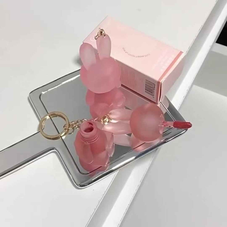 Pink lipstick with keychain on a white surface with a mirror reflection.