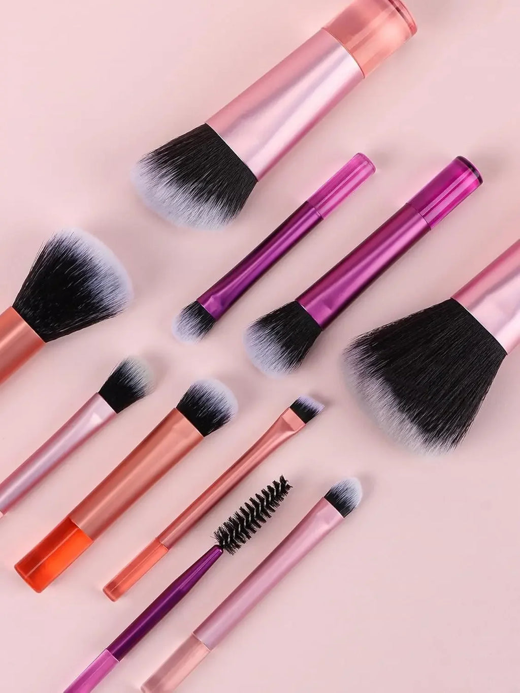 Set of makeup brushes with pink and orange handles on a light pink background