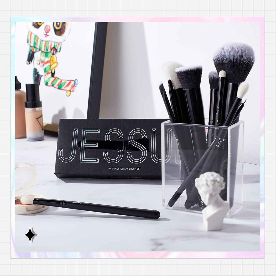 Makeup brushes in a clear holder with a black pouch labeled 'JESSUP' on a white surface.